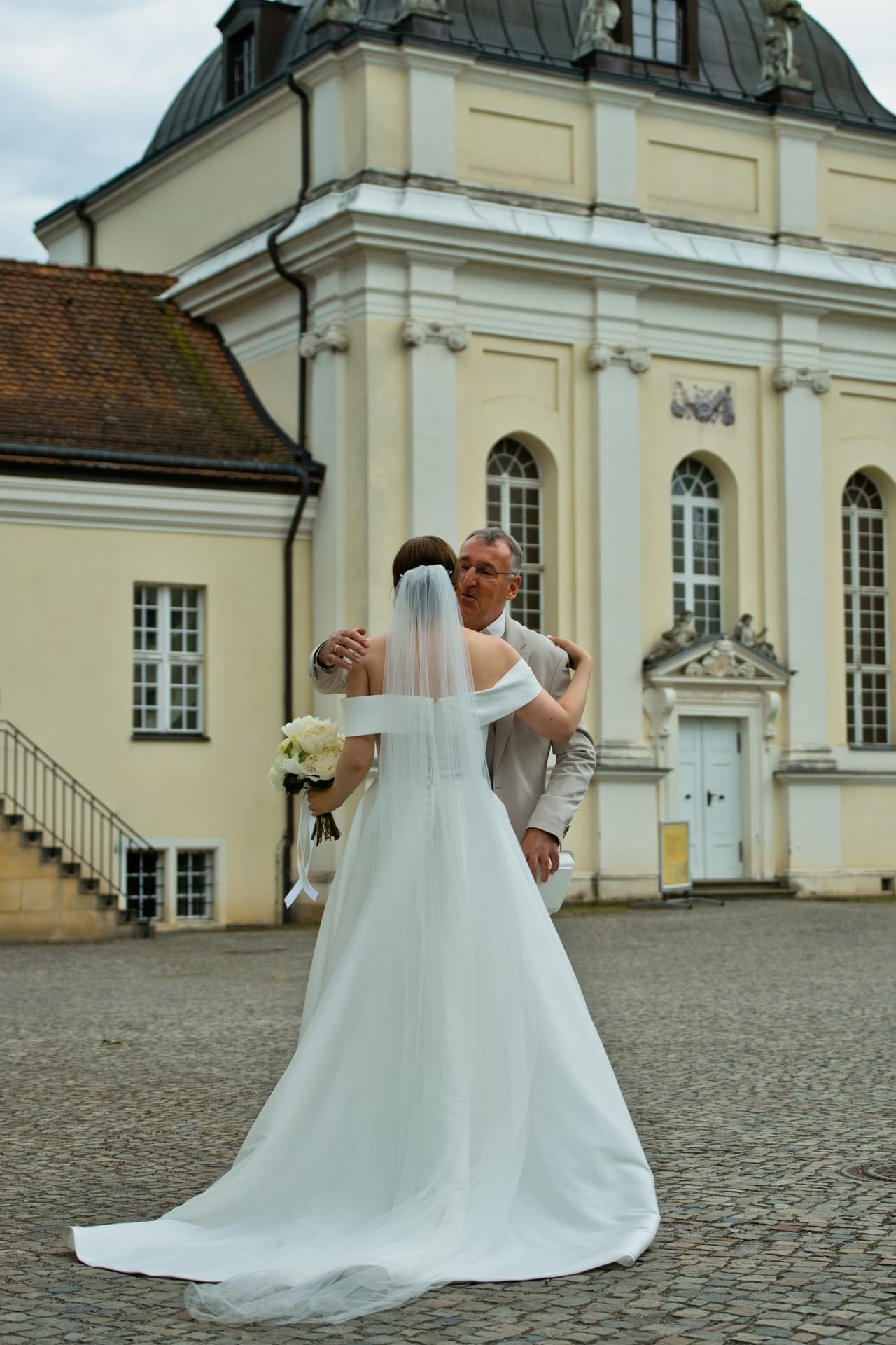Brautvater umarmt die Braut im Hof von Schloss Köpenick