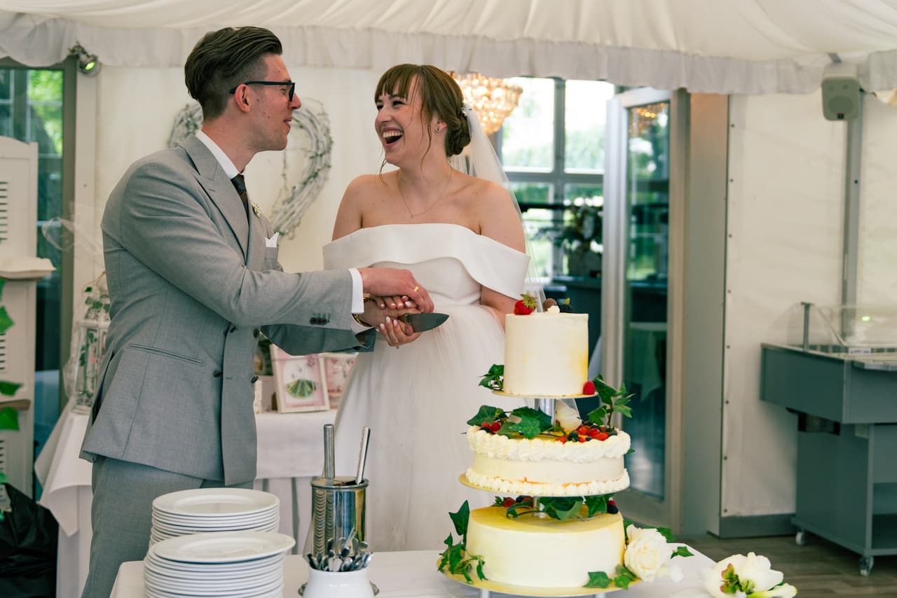 Brautpaar lacht beim Anschneiden der Hochzeitstorte