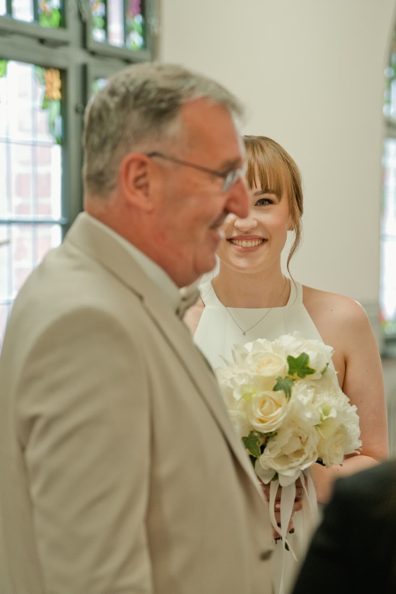 Braut mit weißem Brautstrauß lächelt kurz vor der Trauung – natürliche Hochzeitsfotografie aus Berlin