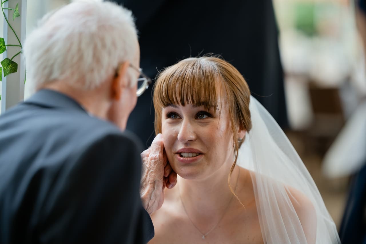 Emotionaler Moment: älterer Hochzeitsgast berührt liebevoll die Wange der Braut