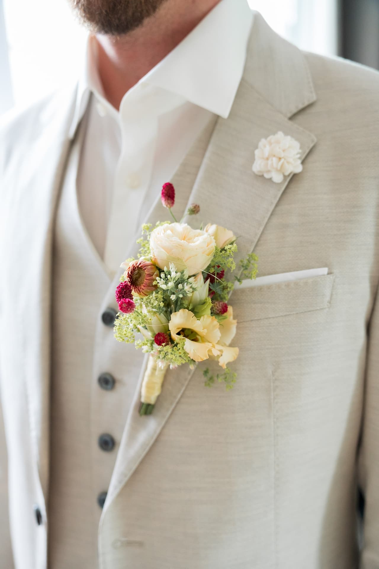 Detail: Ansteckblume mit Rosen und Trockenblumen am beigen Anzug des Bräutigams