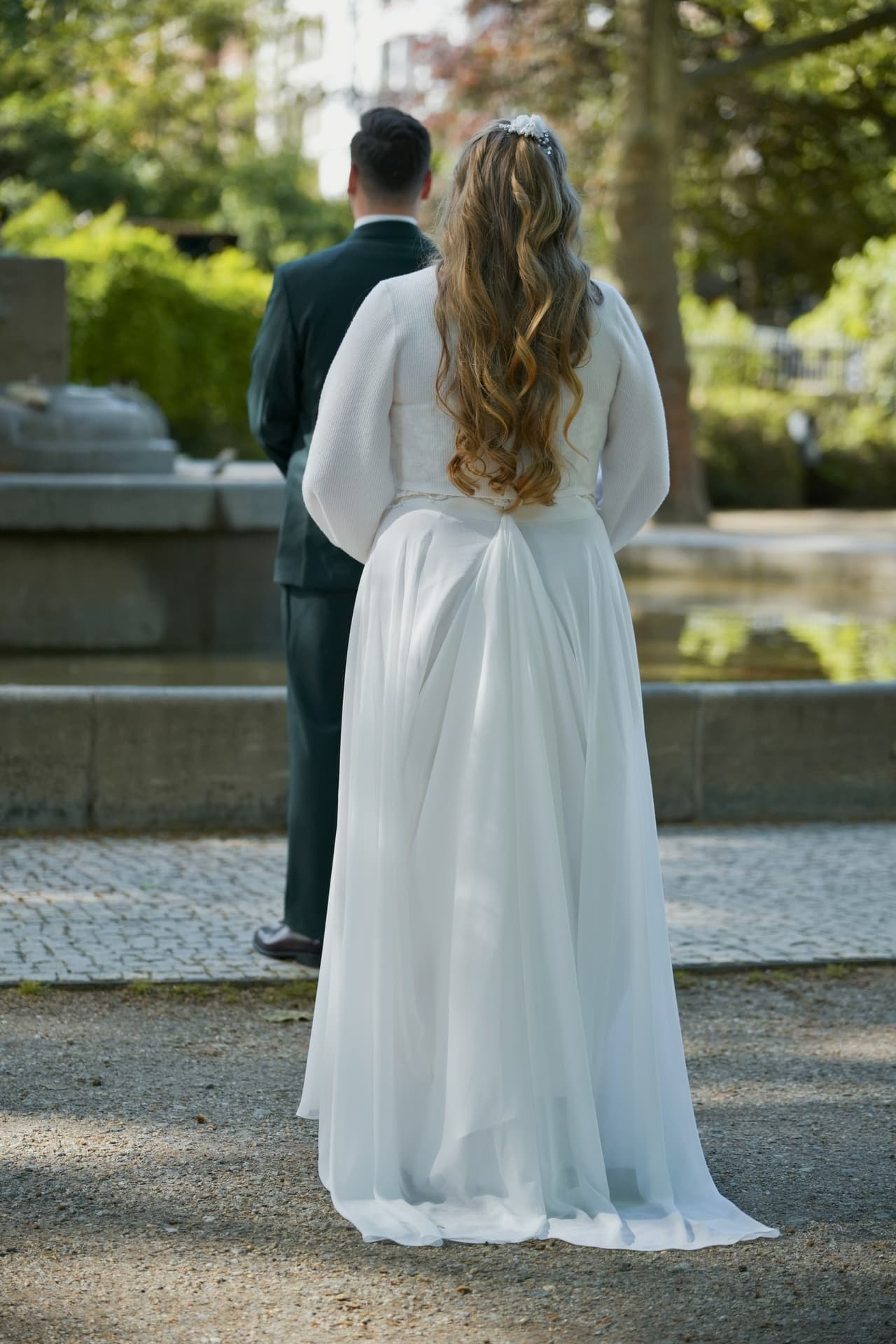 First Look am Brunnen: Braut steht mit dem Rücken zur Kamera vor dem Bräutigam