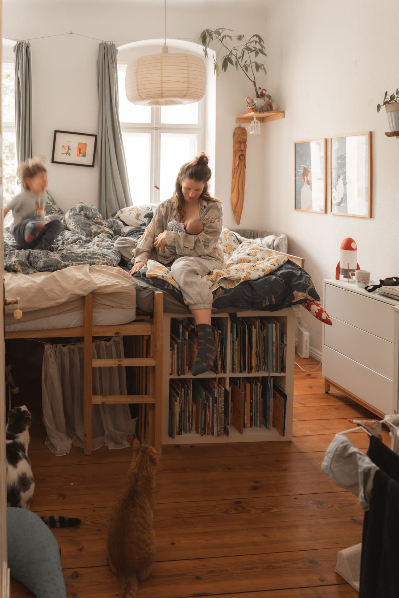 Mutter stillt auf dem Hochbett, unten warten die Katzen – Familienalltag im Wochenbett