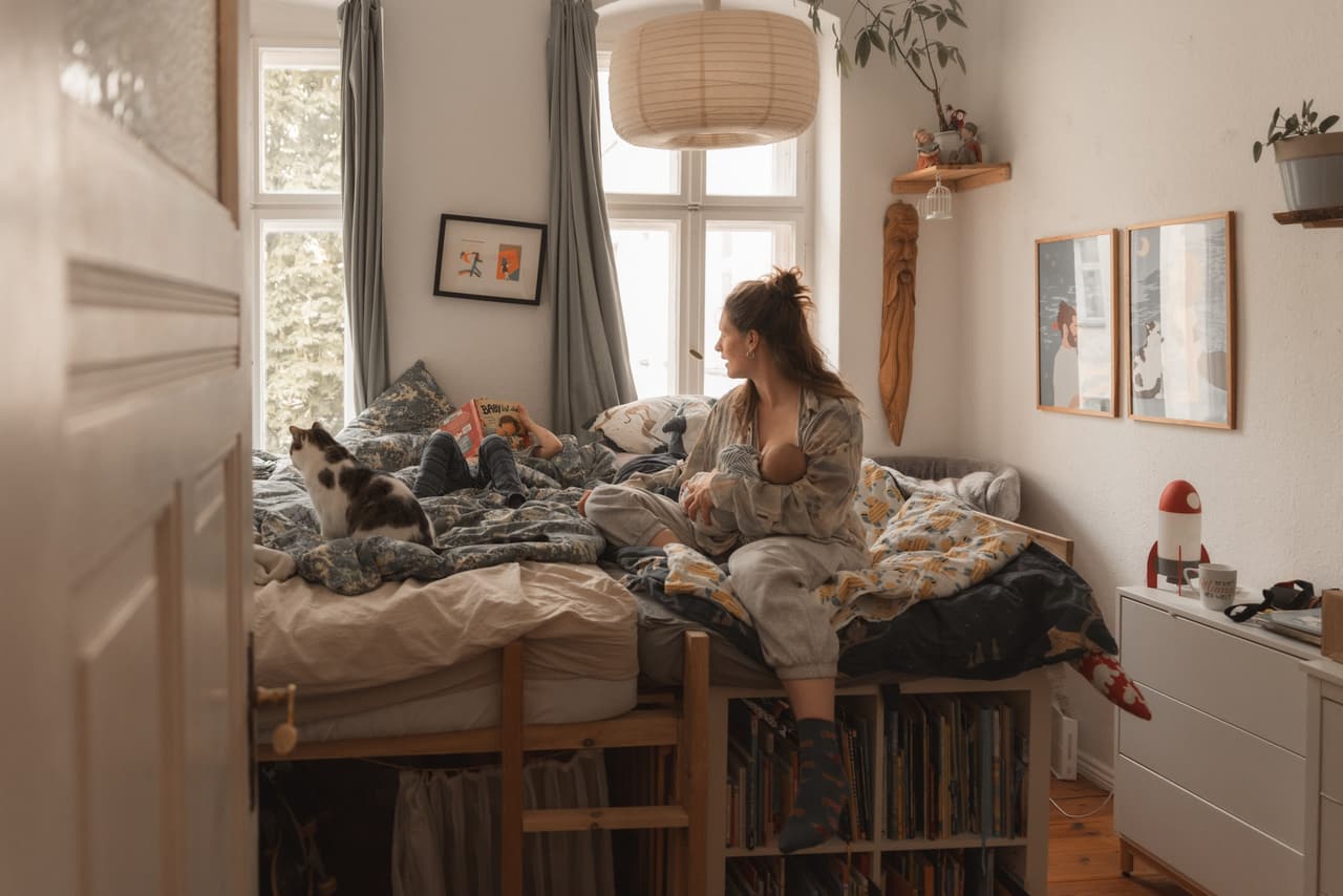 Mutter stillt ihr Baby auf dem Bett, daneben schläft die Katze