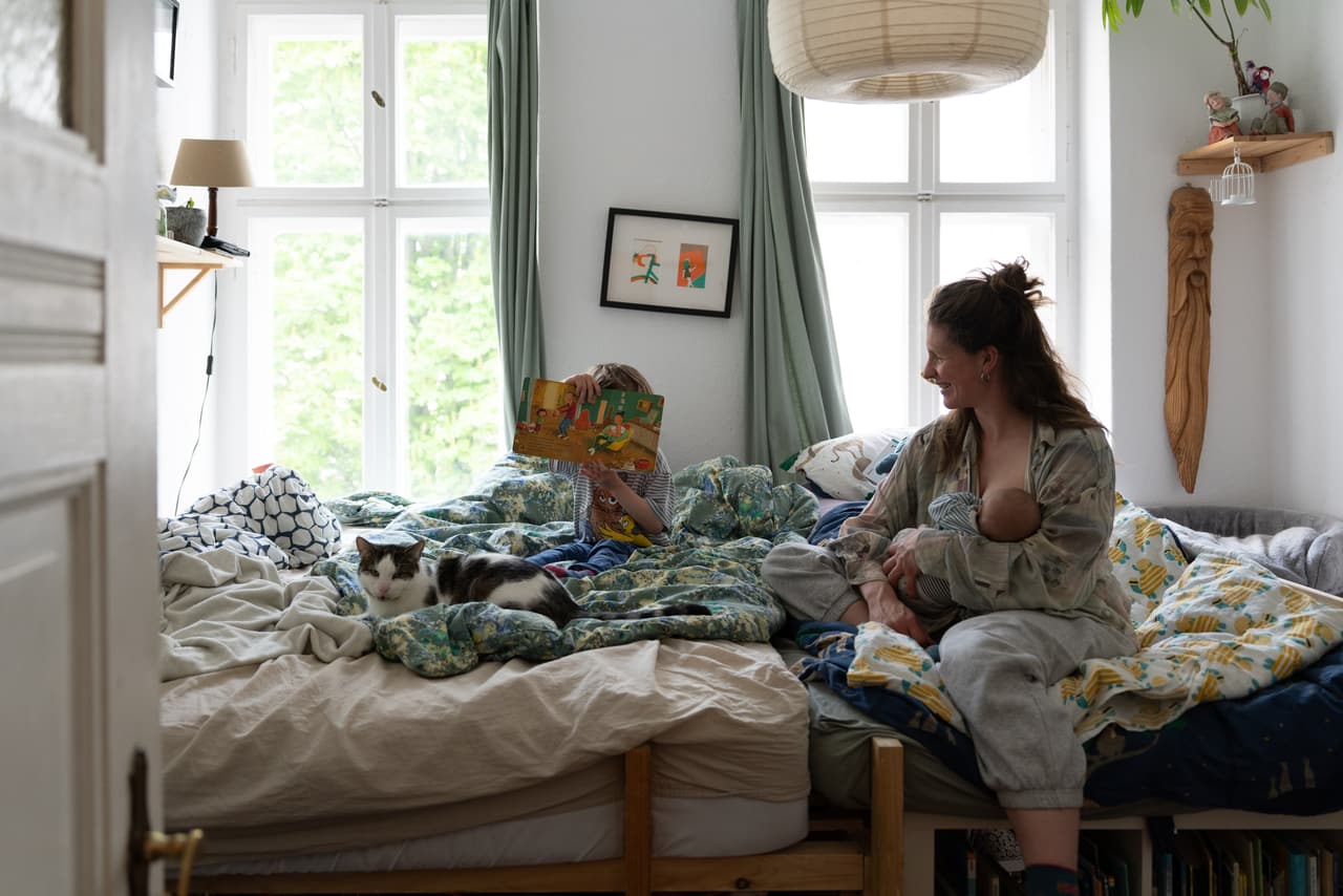 Stillen im Familienbett, das große Geschwisterkind liest ein Buch