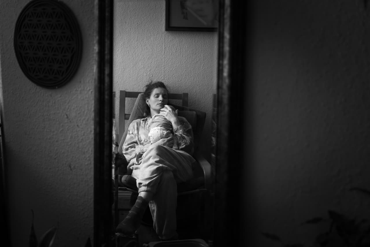 Schwarz-Weiß-Spiegelbild: müde Mutter hält ihr Neugeborenes im Sessel – Wochenbett zu Hause