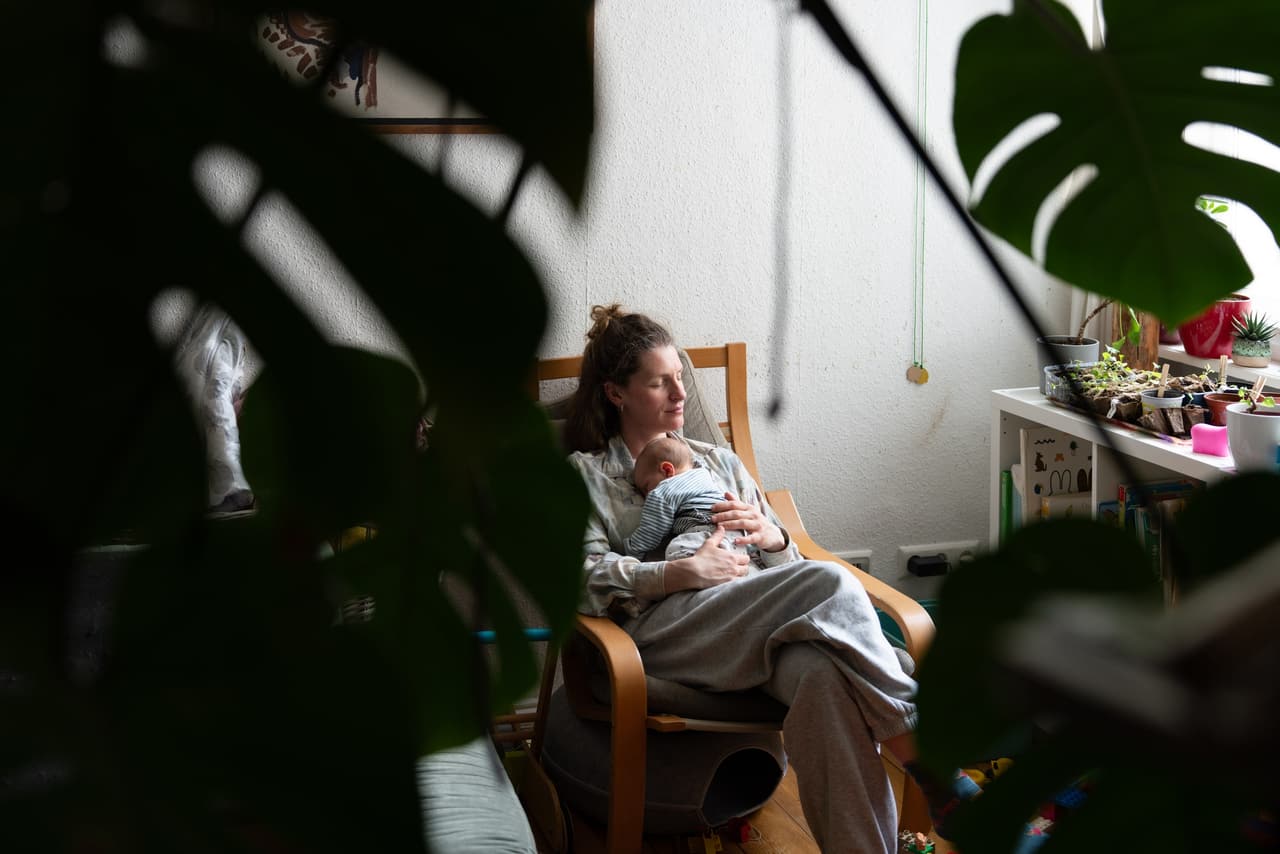 Ruhiger Moment im Wochenbett: Mutter mit Baby im Sessel zwischen Zimmerpflanzen