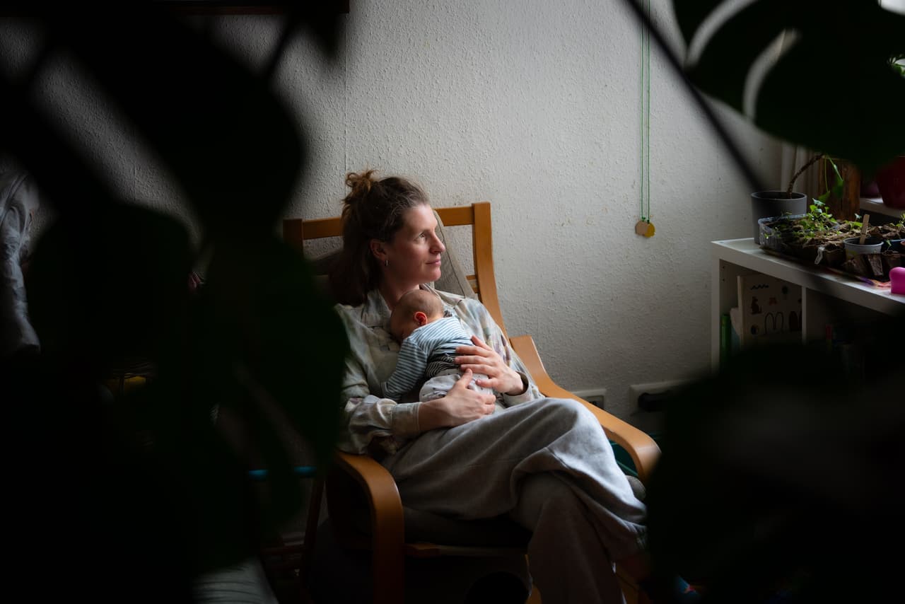 Mutter hält ihr Neugeborenes im Sessel und schaut aus dem Fenster