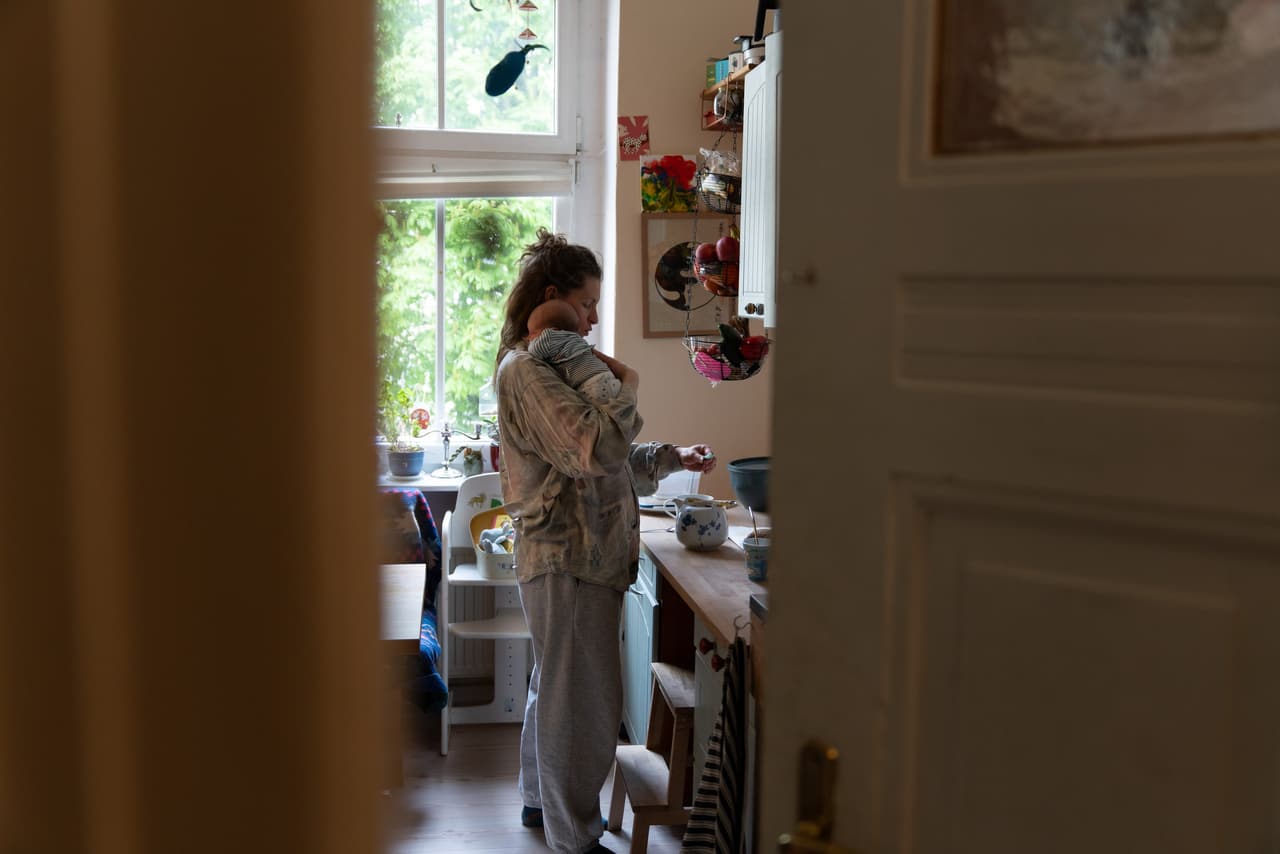 Mutter wiegt ihr Neugeborenes in der Küche, Blick durch die offene Tür